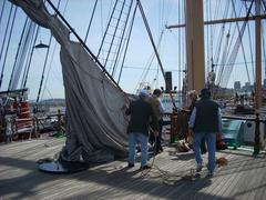 Volunteer canvas crew bending on the newly repaired mizzen staysail on a traditional sailing ship at San Francisco Maritime.