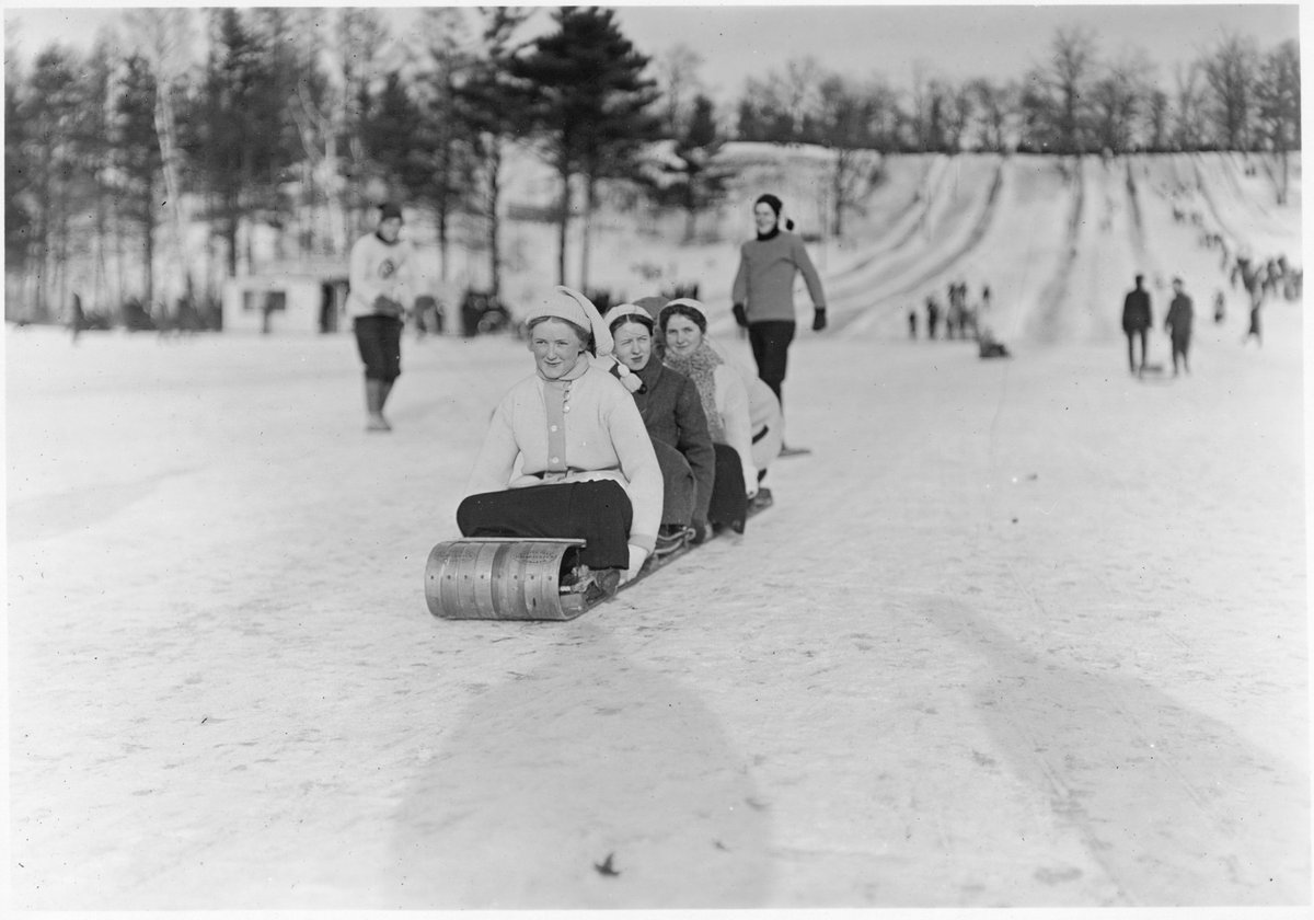Children and adults sledding on toboggan slides in snowy High Park, Toronto