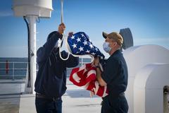 U.S. Navy Sailors and civil service mariners raising the national ensign during morning colors aboard hospital ship USNS Comfort at Naval Station Norfolk