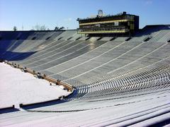 Michigan Stadium covered in snow during winter with empty seats and a foggy sky