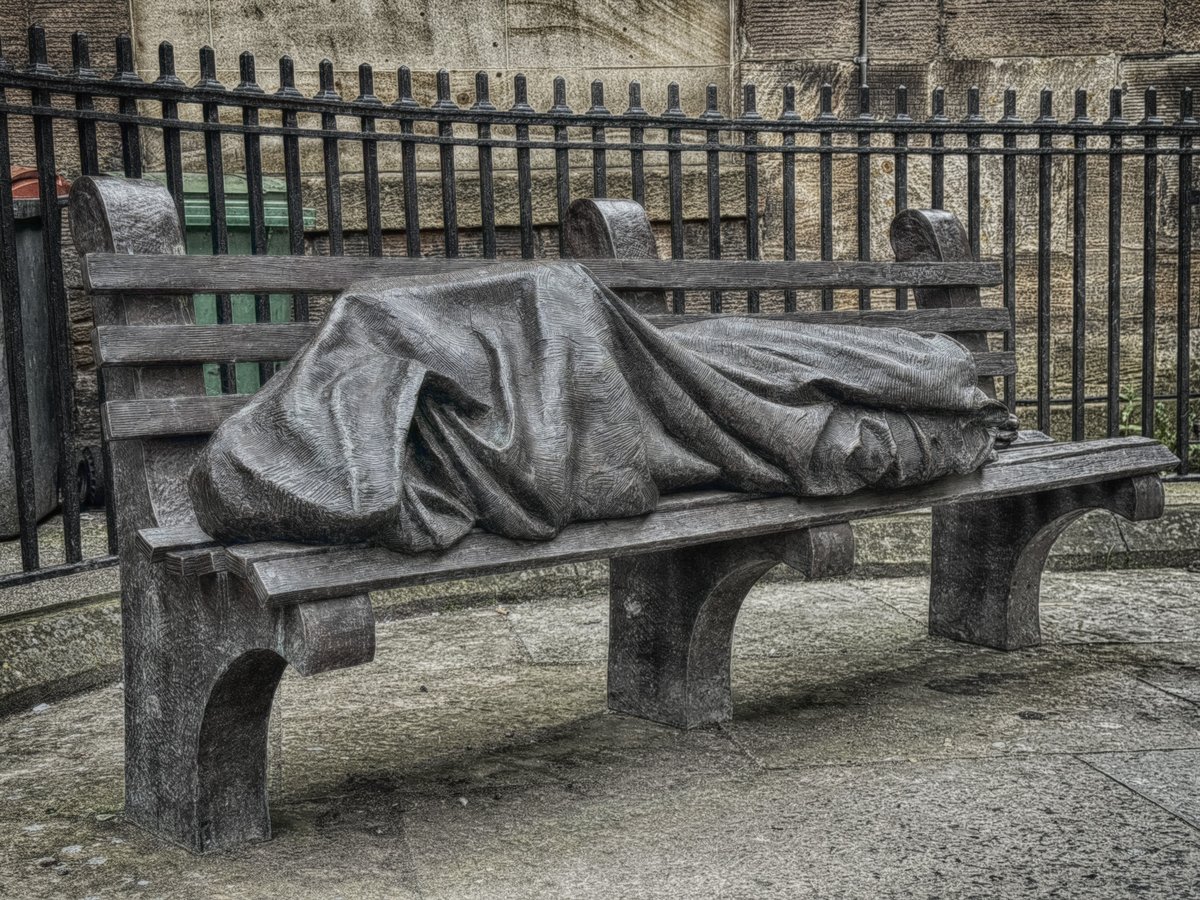 Homeless Jesus sculpture by Timothy Schmalz showing Jesus as a homeless person sleeping on a bench covered with a blanket