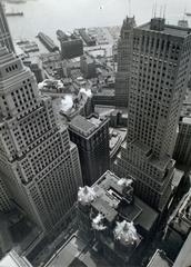 Waterfront view with piers between tall buildings and a low building with domed towers in Manhattan