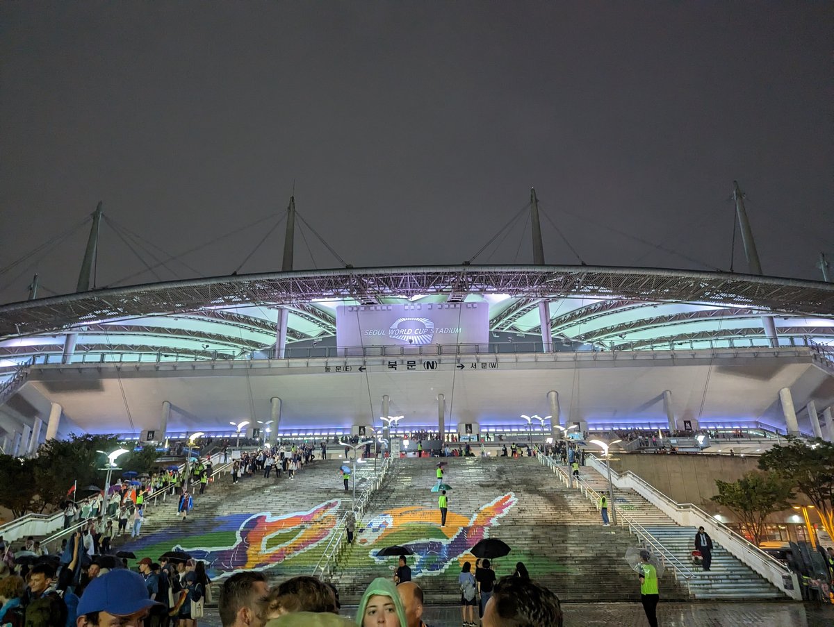 Night view of Seoul World Cup Stadium illuminated after K-pop Super Live closing show 2023 with festival attendees walking down colorful staircase