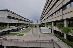 Main entrance of Allgemeines Krankenhaus Wien hospital building with multiple flags and parked cars