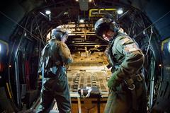 Two U.S. Air Force loadmasters securing safety harnesses before deploying payload over Yokota Air Base