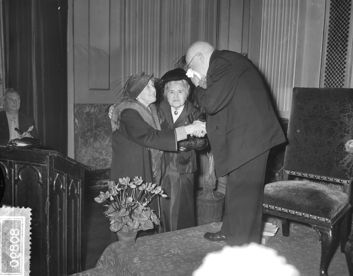 Actor Mari van Warmelo celebrating 90th birthday at reception in Stadsschouwburg foyer with Mien Erfmann-Sasbach and Rika Hopper, black and white photo from 1956