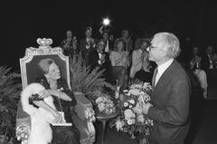 Actress Ank van der Moer sitting on stage listening to Mayor Polak's speech at Amsterdam Stadsschouwburg during her 50th theater anniversary celebration