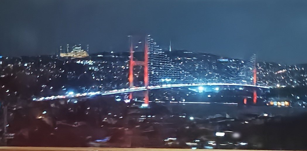 Bosphorus Bridge at night with vibrant lighting spanning over the water and Camlica Mosque illuminated in the background in Istanbul, Turkey