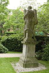 Sculpture of a man holding a pillar under his arm on a pedestal in a garden