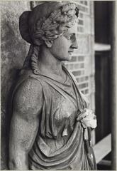 Statue of a woman with one hand on her chest, ornament detail on a building facade