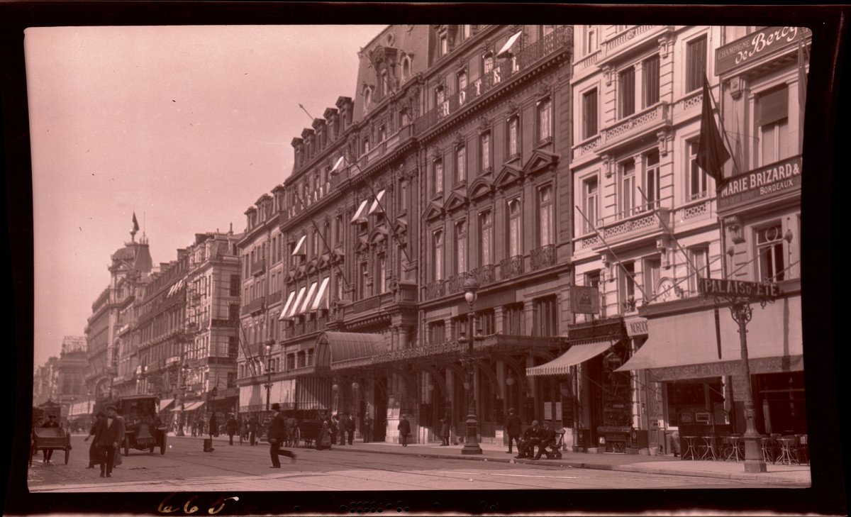 Vintage street scene on Anspach Boulevard in Brussels with pedestrians, carts, and early automobiles passing by the Grand Hotel, which no longer exists