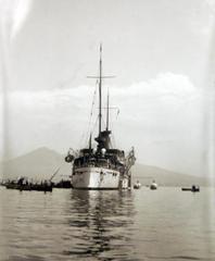 USS Olympia warship docked in Naples harbor in 1899 with buildings visible in the background