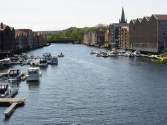 Nidelva river flowing under Gamle Bybro bridge in Trondheim with green trees and buildings along the riverbanks