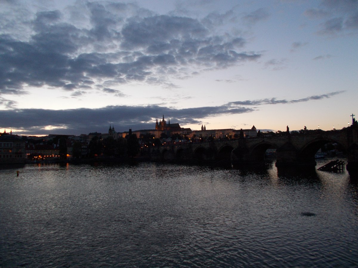 Charles Bridge at dusk over the Vltava River with city lights