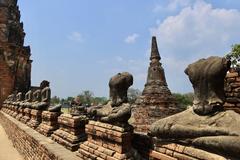 Headless Buddha statues around cloister gallery with bell-shaped stupa in background at Wat Chai Watthanaram temple