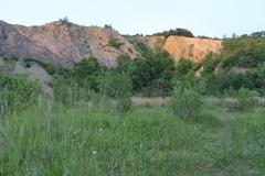 A panoramic view of Růženin lom, a large quarry surrounded by lush green forests and rolling hills under a partly cloudy sky