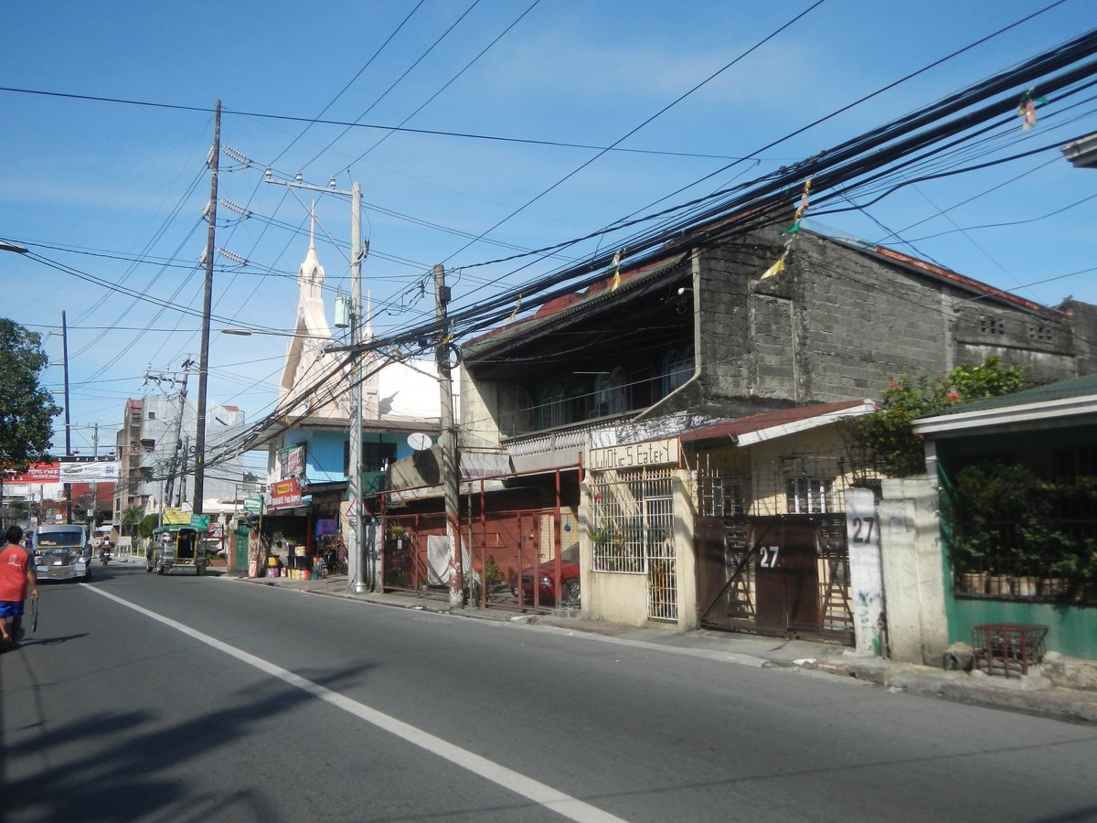 Construction site with Hitachi EX200 excavator on Elpidio Quirino Avenue, Las Piñas and Parañaque City boundary, featuring city welcome arch and surrounding urban landscape