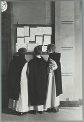 Boys in religious robes at a bulletin board in a Benedictine abbey school during Christmas 1935