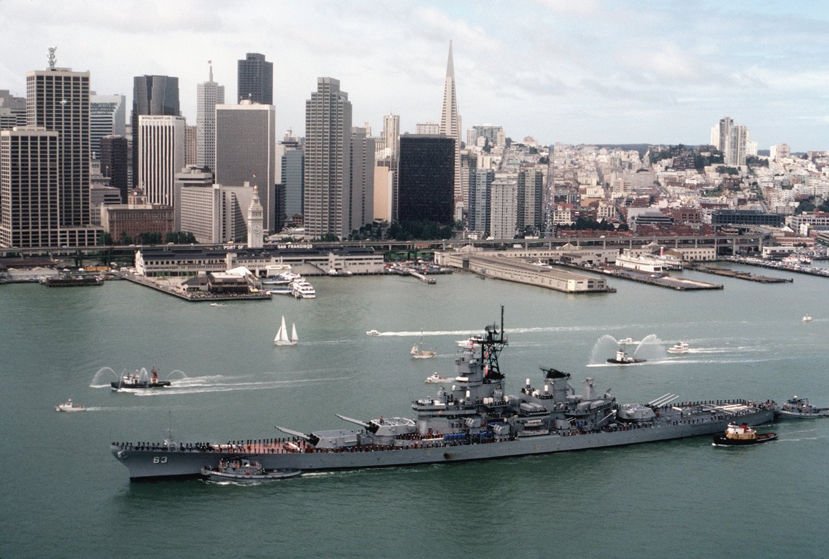 Large harbor tugs assisting battleship USS MISSOURI BB 63 into port with San Francisco skyline in background