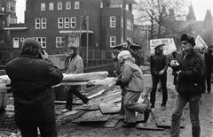 Black and white photo of BBK members demonstrating with incendiary bombs and signs during the first pile driving for the Rijksmuseum Vincent van Gogh construction in Amsterdam on November 25, 1969