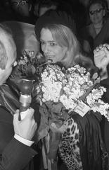 Black and white photo of Melina Mercouri arriving at Amsterdam Central Station wearing a beret and holding a Greek flag on May 14, 1968