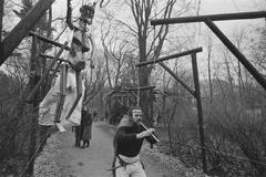Black and white photo of an art exhibition opening in Haags Zuiderpark featuring an artist playing a flute surrounded by gallows-themed artworks