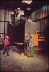 Workmen operating large enclosed sandblasting unit at Avondale Shipyard