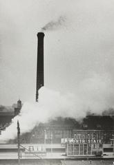 Black and white photo of smoke and soot coming from the chimney of Academisch Ziekenhuis Leiden causing pollution and disturbance to local residents, taken on February 12, 1964
