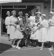 Jan Cottaar standing among nurses at Academic Hospital in Leiden, receiving flowers from his daughter Annemarie, with his wife watching