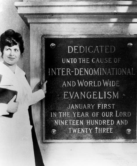 Aimee Semple McPherson standing beside a dedication plaque at Angelus Temple in 1923