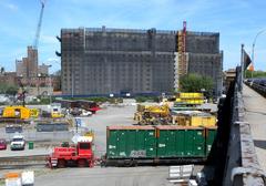 Shuttlewagon towing a train with green containers for municipal solid waste on a sunny day near Willis Avenue Bridge