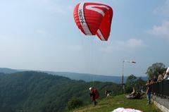 Paraglider taking off from a grassy hill overlooking a forested valley