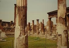 View of ancient ruins in Pompeii with stone buildings and a hill in the background under a blue sky