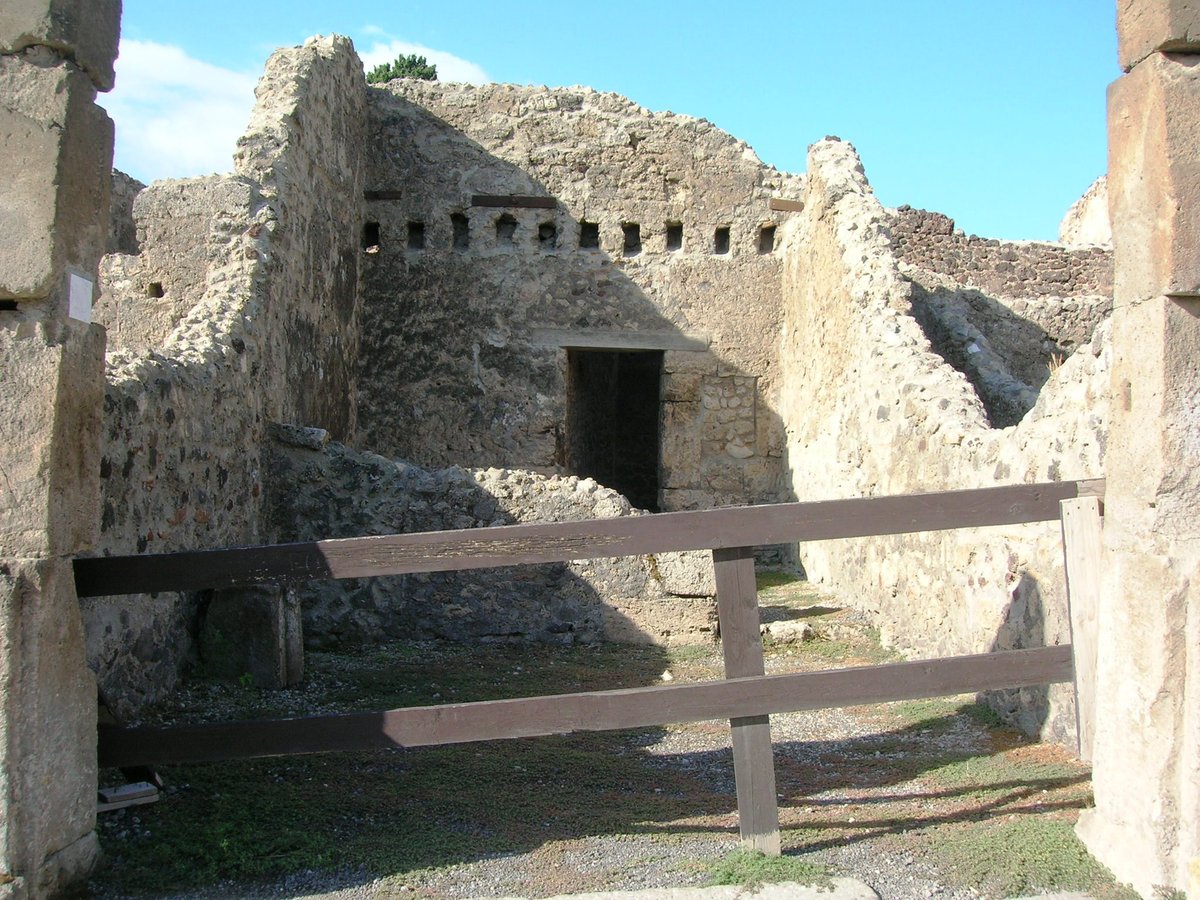 Exterior view of Shop Viii.4.20 in Pompeii with ancient ruins and surrounding plants