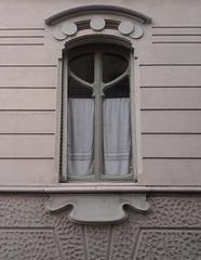 Antique wooden window with intricate iron bars and peeling white paint set in a textured brick wall