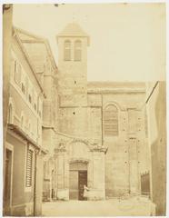 Northern facade of Valence Cathedral during restoration with two-leaf door open and a young girl standing in front, a house with closed shutters on the left