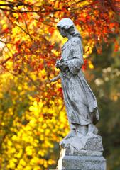 Guardian angel statue above a headstone in Bellefontaine Cemetery during fall