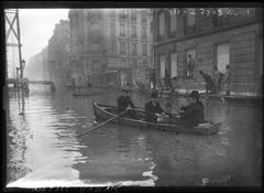 Flooded rue de l'Université in Paris 7th arrondissement with people navigating in boats and on planks supported by stilts during January 31, 1910 flood