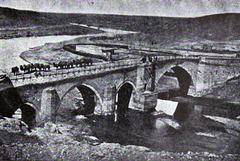 Red Bridge in Yerevan over a river with urban buildings in the background