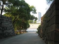 Osaka Castle surrounded by lush green trees under a partly cloudy blue sky