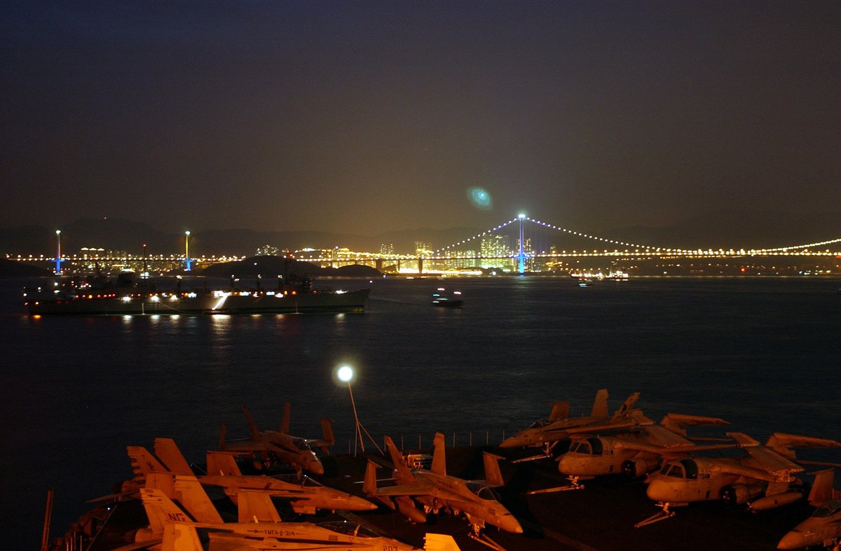 Stern of nuclear aircraft carrier USS Carl Vinson and shadow of Fast Combat Supply Ship USS Sacramento anchored outside illuminated Hong Kong at night