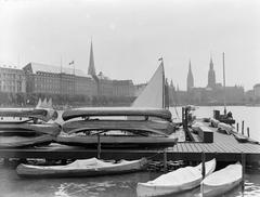 Boats at a pier on Binnenalster lake with the HAPAG office building and towers of St. Petri Church, St. Nikolai Tower, and Hamburg City Hall in the background, 1934