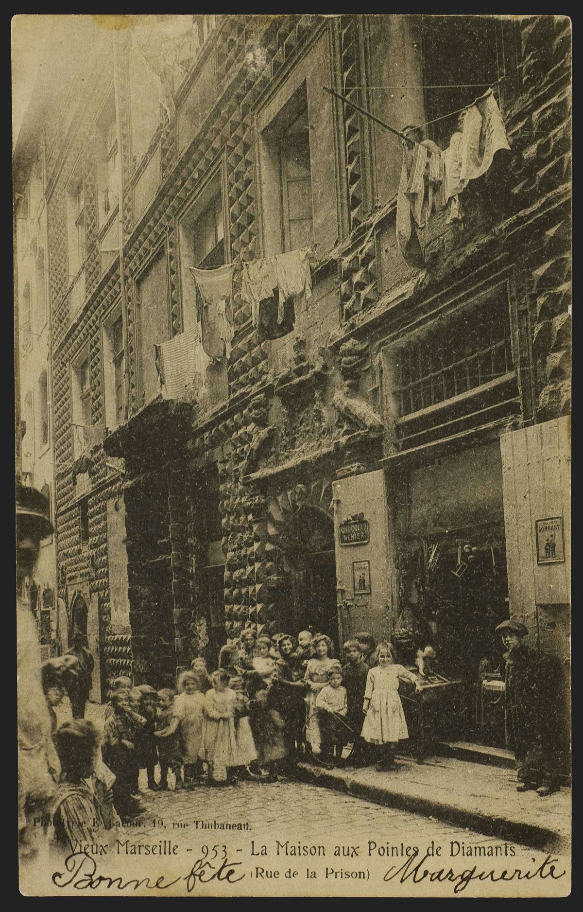 Group of residents and children posing in front of the Maison aux pointes de Diamants on Rue de la Prison in old Marseille, with the storefront of a confectionery visible