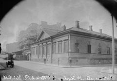 Black and white photo of wooden building at Ritarikatu 10 - Kirkkokatu 11 with Säätytalo under construction in background