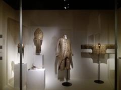 Showcase featuring Cardinal Balthasar Cenci's mitre, a helmet with mobile nasal guard, a flintlock pistol, and 18th century French coat and jacket
