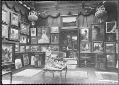 Interior view of Henry Vasnier Gallery room with paintings on walls and floor, sculptures on central table, bookshelves, and rugs on floor