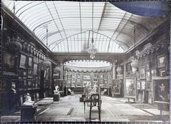 Interior view of a gallery room at Galerie Henry Vasnier with paintings displayed on walls and visitors observing the art
