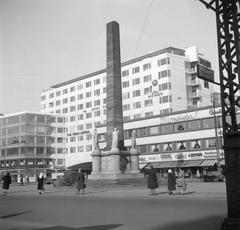 Pedestrians near the 20-meter high Frihedsstøtten monument of freedom from 1797 with shops in the background on Vesterbrogade street in Copenhagen, Denmark in March 1954