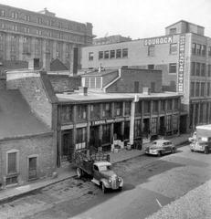 Historical street view of Rue Saint-Pierre in 1947 showing small shops and warehouses against the old church walls in Montreal