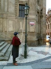 The lamplighter lighting a street lamp on Křižovnické Náměstí square in Prague during autumn 2023